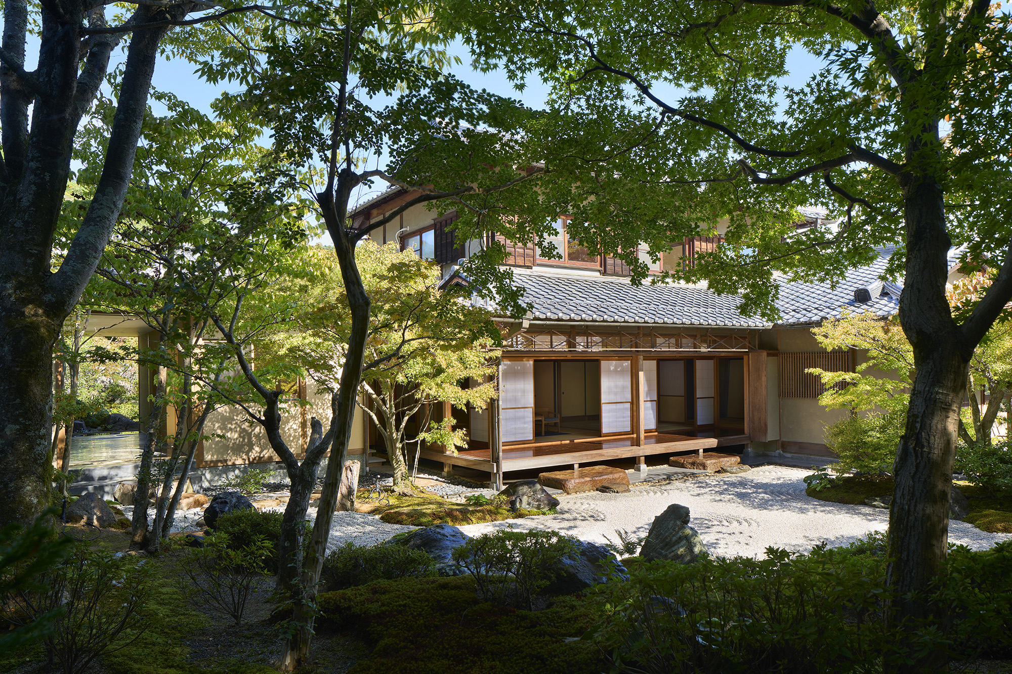 This project involved the renovation of a 50-year-old main house and a detached cottage located in the Oku-Saga area, near the Arashiyama district in Kyoto.
The approximately 1,000-square-meter property features a traditional Zen garden designed by Sone Zouen, a landscape firm known for its longstanding work with the Imperial Household Agency and Zen temples of the Rinzai school.
The main house, a quietly elegant Japanese-style residence, showed traces of being lived in with great care over the years, while the detached cottage had been updated with more modern interior finishes.
The main house was minimally renovated to adapt to the lifestyle of its new residents.
Meanwhile, the detached cottage was fully transformed into a guesthouse, offering a unique and immersive stay experience that resonates with the surrounding Zen garden.
In the main house, we repaired deteriorated parts and updated the plumbing systems to support contemporary living.
Some interior surfaces were selectively renewed using a palette of black materials to subtly tighten the space and minimize visual clutter associated with daily life.
The detached cottage, approximately 43 square meters in area, was completely redesigned as a guesthouse featuring an LDK (living-dining-kitchen) and bath area.
To evoke a sense of spatial richness beyond the compact footprint, we focused on creating a strong connection with the surrounding environment.
Since the cottage is nestled between two gardens on the north and south, we designed the space so that the gardens visually and experientially pass through the building.
Specifically, the LDK was positioned like a tunnel between the gardens and features full-width openings with sliding and folding doors that can be completely opened.
The floor was designed as an extension of the landscape, incorporating traditional stonework with polished cement and embedded stepping stones.
Some stones were polished flat, while others retained their natural textures to offer tactile variation underfoot.
The interior wall finishes were carried over from the exterior to blur the boundary between inside and outside.
Through subtle adjustments in material connections and joinery details, we created a continuous and nuanced transition between garden and architecture.
This was done using a method similar to a “shiritori” word game—where parts are shared, others intentionally varied—allowing garden and building to inform one another.
The bathtub is sunken and frameless, preserving an unobstructed view of the north garden.
By filling the water level up to the floor, the bath surface reflects the garden, creating a “floor of water” that gently extends the presence of the landscape into the interior.
In this project, the garden came first, followed by architectural responses. Then, the garden was refined again in accordance with the architecture.
Through this reciprocal process, the two elements—landscape and architecture—shaped the environment together.
It was a rare and fulfilling experience of collaboration, where each complements the other to form a cohesive and resonant space.