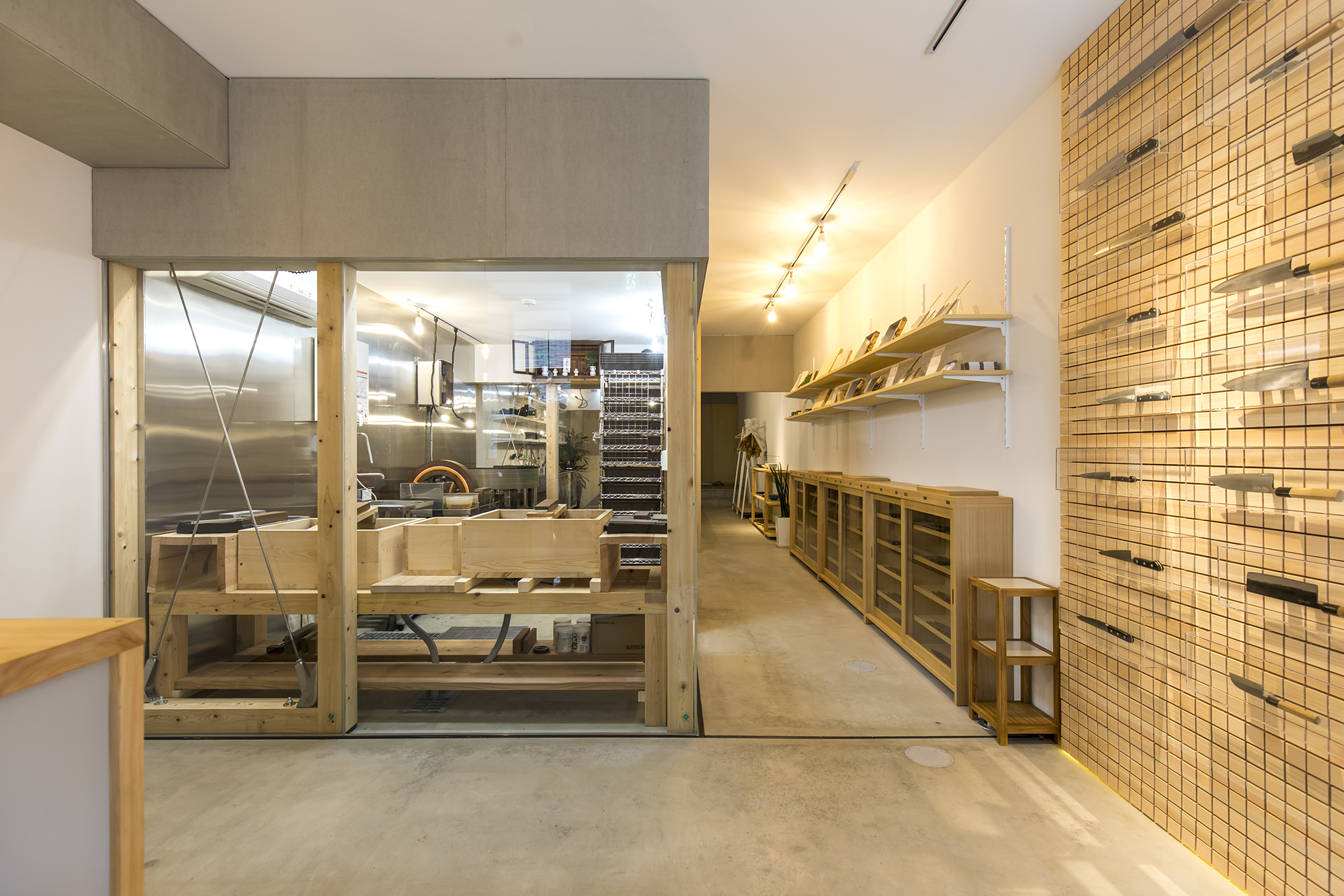The existing two-story residential building is a typical house in the city of Kyoto with a narrow frontage and a long depth. The renovation of the first floor into a store with a workshop space in the dense suburban district, surrounded by wooden houses, was challenging in various ways: the noise from the working space to the neighborhood, requirement of an open space due to the various spatial uses, and the static restriction of the existing wooden construction. All the aspects seemed to be contradictory to each other.
The main concept of the store was to create not only a sales place but also a room, where various courses were to be held. It is their main philosophy to strive for passing on the invisible cultural values through letting people work with tools, by giving knife maintenance courses and cooking classes among the others.
In order to embody the concept of the store, a rather openly designed box-shaped workshop, called LABO, was placed in the center of an elongated room with 4.0m width and 15.5m depth. It divides the floor in three spaces with the sales place in front and the kitchen in back.
The knives are bladed, maintained, and repaired in LABO. Visitors are able to take a close look at the work of craftsmen here, even how they engrave knives with their names. Lectures and classes are held in the kitchen.
The composition of architecture and furniture in this project should have the same simplicity as that of the kitchen knife: a blade, a metal base, and a handle.
In relation to the operating order, such as grasping and placing, we tried to put links between tools, furniture, and architecture as much as possible.
A steel angle profile with a magnet and felt is inserted in slits of the wooden wall panel. The knife is held magnetically and the acrylic case by the felt. The display layout can be rearranged flexibly and each knife can be taken out easily.
As for the interior, it was intentional to use common materials with ingenuity and to finish in a simple and pragmatic manner. In this way, it appears that kitchen knives and other utensils in higher quality are not mainly luxury displays, but rather something that can make one’s everyday life richer.
You might learn more about a culture by having a hand-crafted kitchen knife. The same could happen by dealing with furniture, architecture and even cities. It would be wonderful if a city became a platform that would mediate the thoughts of people.
translated by Tota Goya